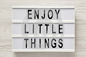 `Enjoy little things` words on a modern board on a white wooden background, top view. Overhead, from above, flat lay. Close-up