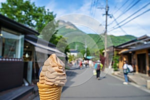 Enjoy melting chocolate ice cream soft serve cone on local street in spring with blurred people, mountain and blue sky background