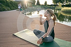 Enjoy the moment. Attractive middle aged woman drinking water while doing yoga on a mat in a green park