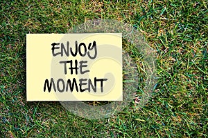 Enjoy the moment message written on paper on grass background. Inspirational quote for positive happy memorable times