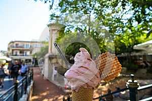 Enjoy sparkled melting pink strawberry ice cream soft serve cone and crispy waffle along sidewalk with blurred people background photo