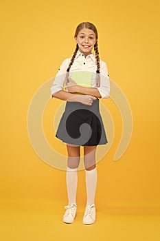 Enjoy studying. Exciting literature. Girl child hold book stand yellow background. Schoolgirl studying textbook. Kid