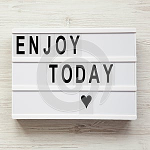 `Enjoy today` word on lightbox over white wooden background, from above. Top view, overhead, flat lay.
