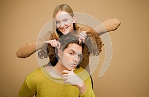 Enjoy twogether. A blonde girlfriend making funny hairstyle to her boyfriend with curly hair. Young couple doing a joke