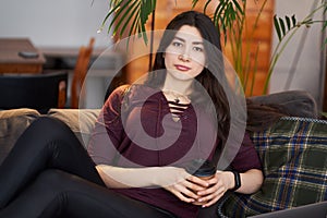 Enjoy weekend. Asian girl relaxing, drinking coffee and sitting on a couch