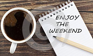 ENJOY THE WEEKEND text on notebook with coffee on wooden background