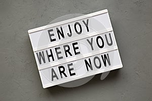 `Enjoy where you are now` words on modern board over concrete surface, top view. Flat lay, from above. Close-up