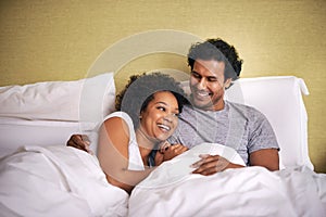 Enjoying a cuddle with the hubby. A young husband and wife lying bed together.
