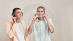 Enjoying favourite playlist. Two young caucasian twin brothers in casual wear listening music in headphones and wireless