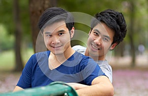 Enjoying the freedom to be themselves. Cute young gay Asian couple smiling together while sitting in the park.