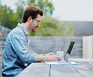 Enjoying the freedoms of freelancing. Shot of a handsome young man using a laptop outdoors.