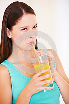 Enjoying a fresh glass of orange juice. Portrait of a beautiful young woman drinking orange juice through a straw.