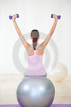 Enjoying a full workout session. Rearview shot of a young woman sitting on an exercise ball and doing some strengthening