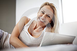 Enjoying a good read online. a mature woman using her digital tablet while lying in bed.