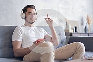 Enjoying his favorite music. Cheerful young man in headphones listening to the music while sittng on his couch at home.