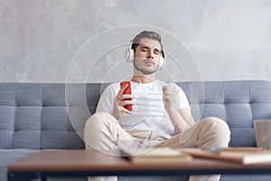 Enjoying his favorite music. Cheerful young man in headphones listening to the music while sittng on his couch at home.