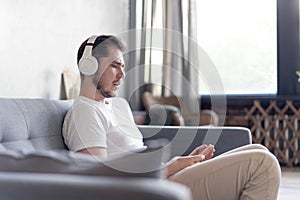 Enjoying his favorite music. Cheerful young man in headphones listening to the music while sittng on his couch at home.