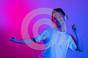 Enjoying his favorite music. Happy young stylish man with headphones listening and smiling while standing against blue neon