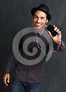 Enjoying his music. Portrait of a hip young man listening to music and showing you his cellphone.