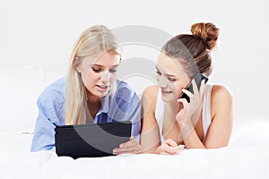 Enjoying the latest gadgets. A beautiful young woman talking on her smartphone while her friend uses a tablet while