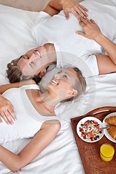 Enjoying a lie-in with breakfast. Cropped view of a young couple lying in bed alongside their breakfast and looking up.