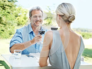 Enjoying a lunch date. Happy mature couple toasting their love with two glasses of wine while outdoors.