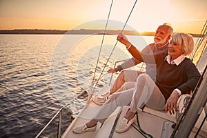 Enjoying luxury life. Beautiful happy senior couple in love relaxing on the side of sailboat or yacht deck floating in