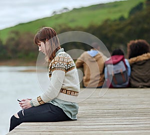 Enjoying a moment to herself. a young woman sending a text message while sitting on the pier by a lake.