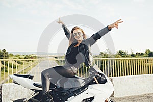 Enjoying moment woman biker posing with hands up sitting on a mo