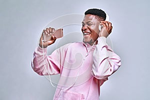 Enjoying the music. A handsome African-American is dressed in a pink hoodie and stylish belvede headphones holding a phone and