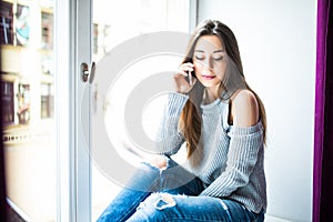 Enjoying nice talk. Attractive young woman talking on the phone while sitting on window sill