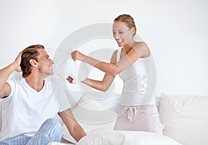 Enjoying a pillow fight. A young couple wearing pjamas and having a pillow fight together.