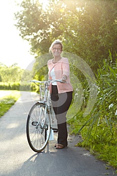 Enjoying a refreshing day out - Bicycling. Attractive senior woman standing on a country lane with her bicycle.