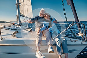 Enjoying sailing. Happy lovely senior family couple hugging and relaxing on a sail boat or yacht deck floating in a calm