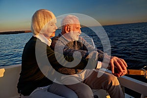 Enjoying sailing together. Side view of beautiful senior couple, elderly man and woman sitting on the side of sailboat