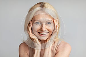Enjoying self-care routine. Happy beautiful caucasian mature woman posing over light grey background
