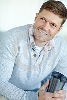 Enjoying some fresh coffee. A handsome mid adult man sitting at home and holding a travel coffee mug and smiling.