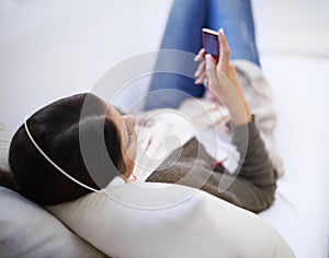 Enjoying some tunes. A young woman listening to her mp3 player while lying on the sofa.