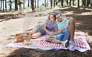 Enjoying the summer sun together. View of a happy young couple enjoying a summer picnic in the forest.