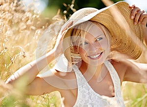 Enjoying the summer sunshine. Beautiful young woman wearing a straw hat and standing in a field.