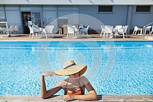 Enjoying summer vacation at tropical resort. Beautiful carefree woman in hat relaxing in pool.Travel