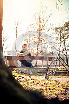 Enjoying the sun in spring: Young girl is sitting on park bench, bicycle back view