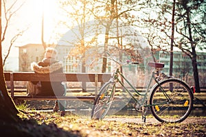 Enjoying the sun in spring: Young girl is sitting on park bench, bicycle back view