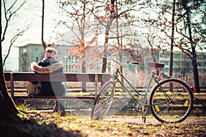 Enjoying the sun in spring: Young girl is sitting on park bench, bicycle back view