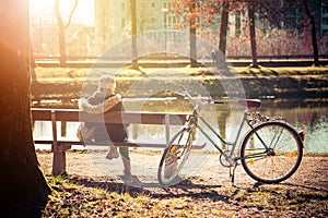 Enjoying the sun in spring: Young girl is sitting on park bench, bicycle back view