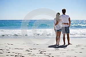 Enjoying the sunshine. Back view of a couple with their arms around each other looking at the ocean.