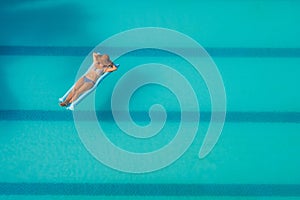 Enjoying suntan. Vacation concept. Top view of slim young woman in bikini on the blue air mattress in the big swimming pool