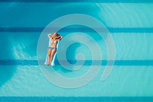 Enjoying suntan. Vacation concept. Top view of slim young woman in bikini on the blue air mattress in the big swimming pool
