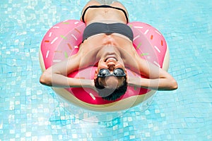 Enjoying suntan woman in black bikini on the inflatable mattress in the swimming pool