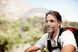 Enjoying a thoughful moment out in nature. Handsome male hiker smiling while seated on a mountain top.